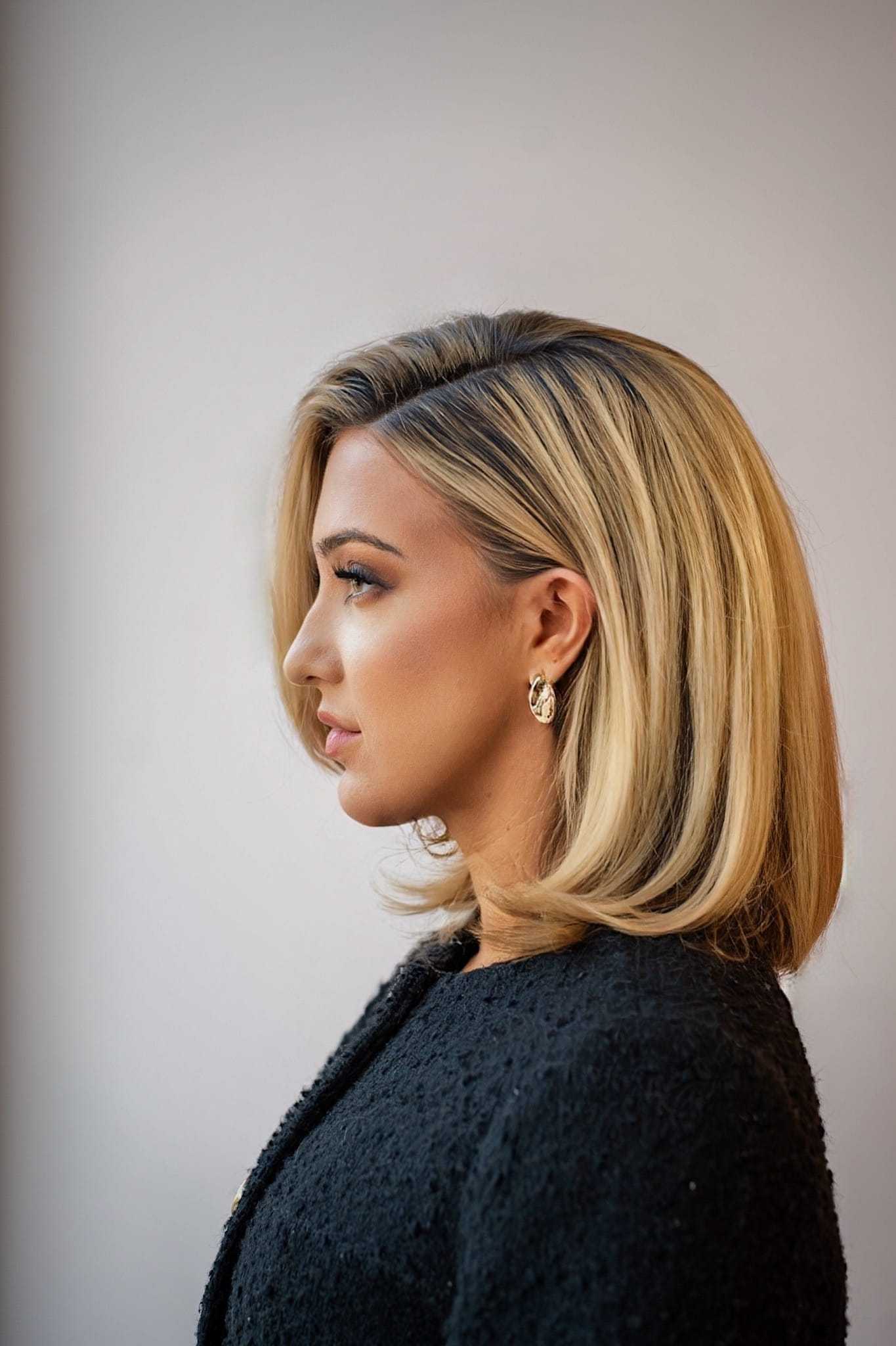 Profile of a woman with blonde hair and gold earrings, wearing a black textured outfit.