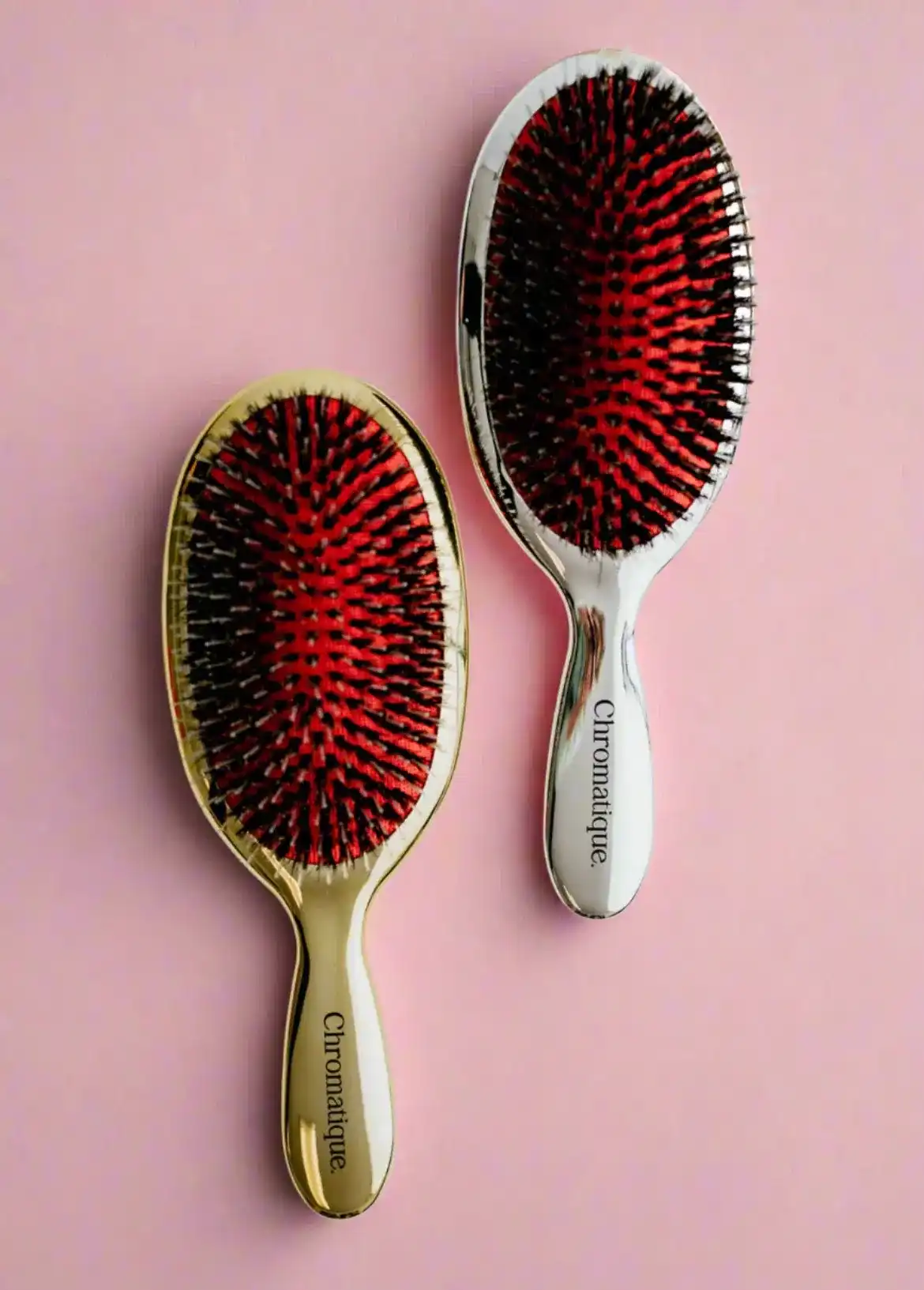 Two Chromatique hairbrushes with red bristles on a pink background.