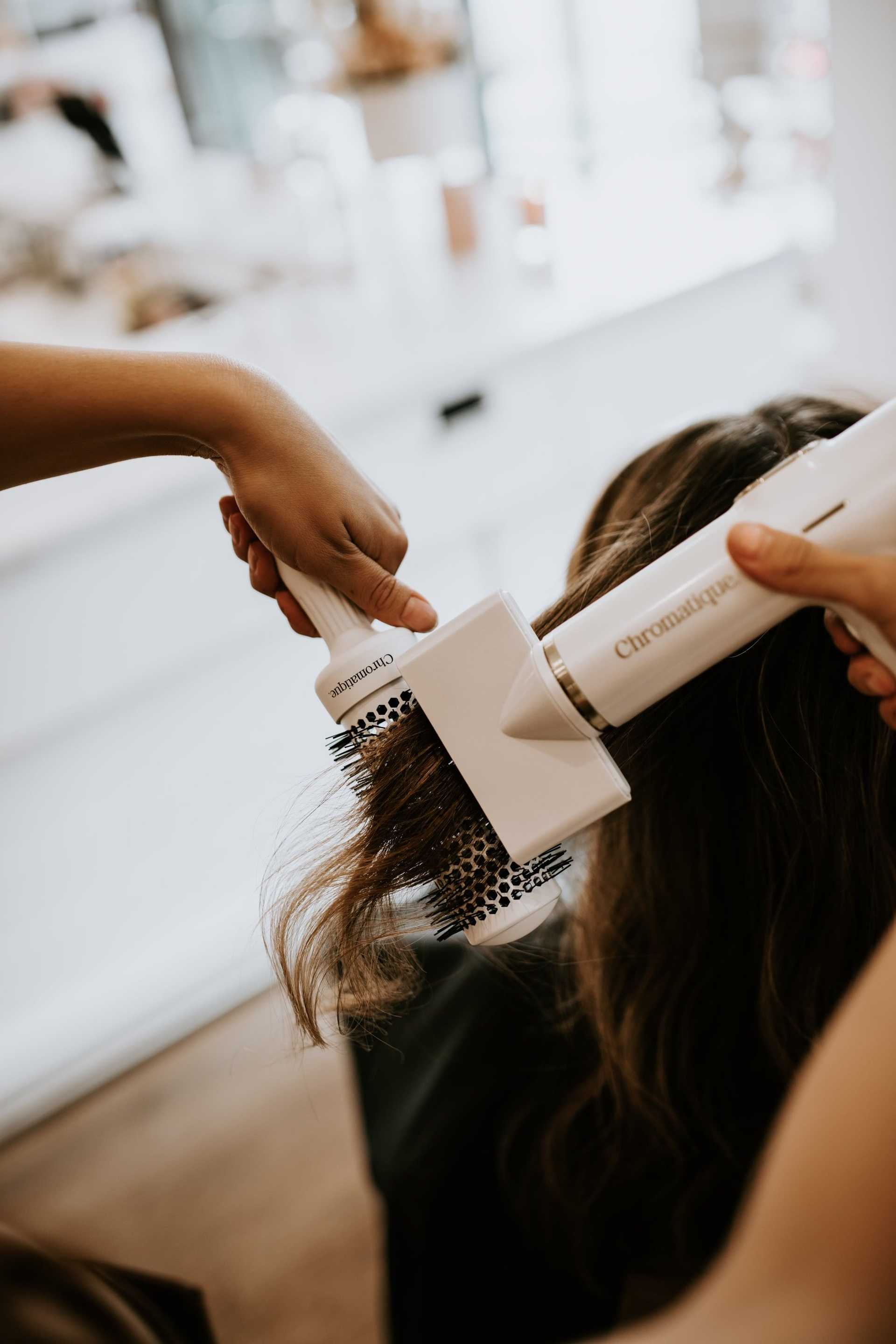 Hair stylist curling client's hair with a round brush and heat styling tool.